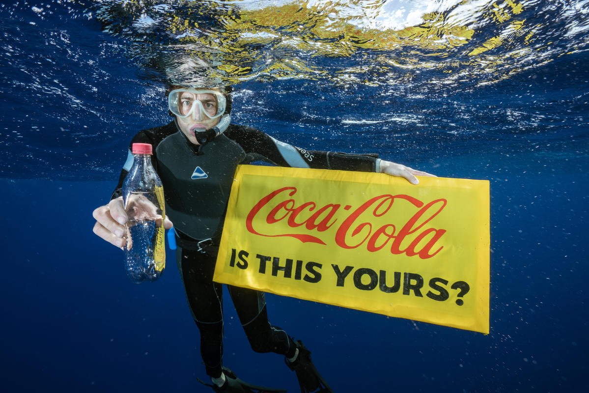 A Greenpeace diver holds a banner reading "Coca-Cola is this yours?" and a Coca-Cola bottle found adrift in the garbage patch.